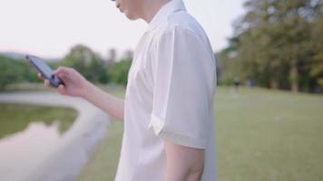 cierra las manos de un hombre tocando la pantalla del teléfono mientras se relaja caminando en un parque natural, baja la cabeza usando un dispositivo portátil de tecnología de la información, actividad recreativa al aire libre, la gente se conecta al concepto video