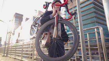 atractivo empresario relajante que lleva su bicicleta en el hombro. ir al lugar de trabajo, moderno edificio de oficinas en el fondo. utilizando el paso elevado para reducir los accidentes de tráfico, la vida de la ciudad, el concepto de ecología. video