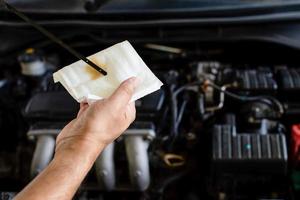 Concept of engine maintenance. A technician is checking the level of the engine oil. Man holding white tissue paper to wipe the engine oil. Close up, Blurred background photo