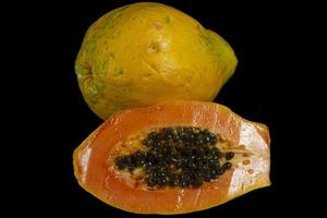 medio corte de papaya madura fresca con semillas aisladas sobre fondo oscuro. enfoque selectivo. foto