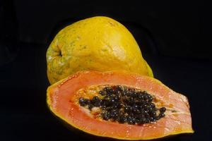 medio corte de papaya madura fresca con semillas aisladas sobre fondo oscuro. enfoque selectivo. foto