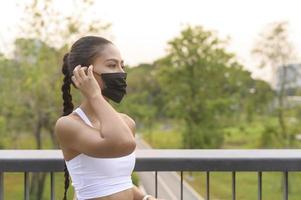 mujer joven fitness en ropa deportiva tomando mascarilla mientras hace ejercicio en el parque de la ciudad, salud y estilos de vida. foto