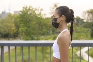 mujer joven fitness en ropa deportiva tomando mascarilla mientras hace ejercicio en el parque de la ciudad, salud y estilos de vida.