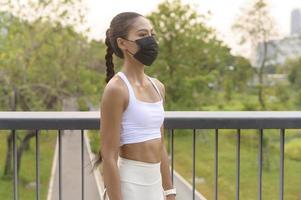 mujer joven fitness en ropa deportiva tomando mascarilla mientras hace ejercicio en el parque de la ciudad, salud y estilos de vida.