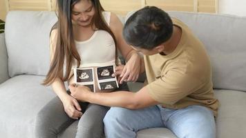 joven mujer embarazada con su esposo sosteniendo una foto de ultrasonido del bebé recién nacido, la maternidad y el concepto de familia