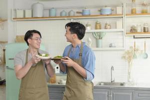 Young smiling gay couple cooking together in the kitchen at home, LGBTQ and diversity concept. photo