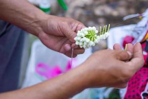 Close-up of man hands using a needle for making jasmine garland. photo