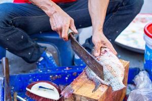 el trabajador está cortando pescado de tilapia en el mercado fresco foto