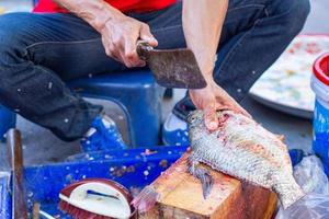 el trabajador está cortando pescado de tilapia en el mercado fresco foto