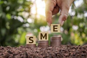 SME Startup Idea Hands puts a wooden block labeled SME on a pile of money growing from the ground. photo
