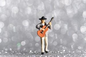 Músico en miniatura con guitarra sobre fondo bokeh foto