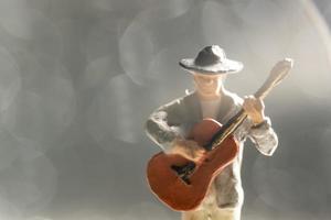 Músico en miniatura con guitarra sobre fondo bokeh foto