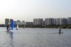 Windsurfer. Man is surfing on the background of skyscrapers. Man on a windsurf board. Windsurfing in the city. Water sports. Surfing with a sail. Windsurfing equipment. Active lifestyle.