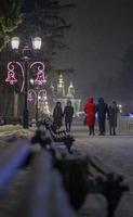 foto de cerca de una farola en la oscuridad en invierno con copos de nieve cayendo. calle decorada para navidad y año nuevo. atmósfera mágica de la tarde. calle de noche. alumbrado público retro.