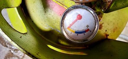 An old and dull gas meter on the green gas cylinder under the dim light background photo