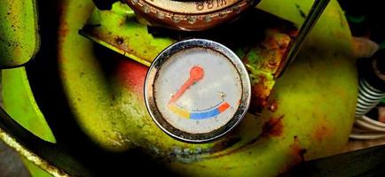 An old and dull gas meter on the green gas cylinder under the dim light background photo