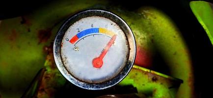 An old and dull gas meter on the green gas cylinder under the dim light background photo