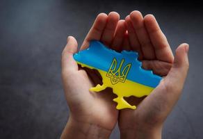 manos sosteniendo la forma de la frontera de Ucrania con bandera de color foto