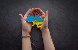 Hands holding the shape of Ukraine border with color flag photo