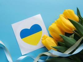 Card with a heart in the colors of the Ukrainian flag and yellow tulips on a blue background photo