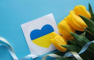 Card with a heart in the colors of the Ukrainian flag and yellow tulips on a blue background photo