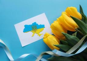 Card with a map of Ukraine in the colors of the Ukrainian flag and yellow tulips on a blue background. photo