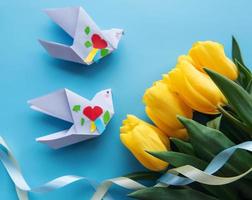 Yellow tulips and origami paper birds on a blue background photo