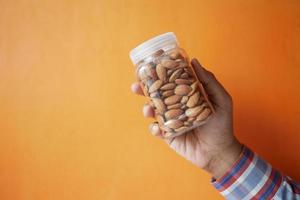 holding a almond nuts jar against orange background photo