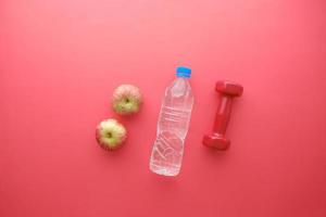 fresh drinking water, apple and a pink color dumbbell on red photo