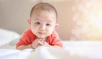 Happy family, Cute Asian newborn baby wear red shirt lying, crawling, play on white bed look at camera with happy face. Little innocent infant adorable child in first day of life. Mother Day concept.