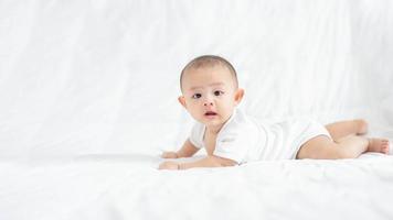 familia feliz, lindo bebé asiático recién nacido acostado jugar en la cama blanca mira la cámara con una sonrisa sonriente cara feliz. pequeño inocente nuevo bebé adorable niño en el primer día de vida. concepto del día de la madre. foto