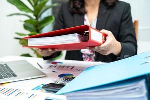 Asian accountant holding binder and working  analyzing financial project accounting with chart graph and laptop in modern office, finance and business concept. photo