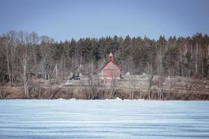 Old house standing on lake bank covered in snow photo