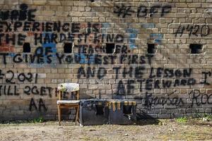 Black paint writings on yellow brick wall with chair standing near and long shadows photo