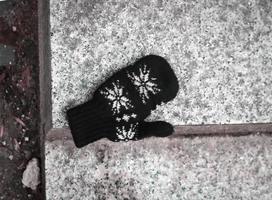 Black wool mitten with white ornament left on marble stairs outdoors photo