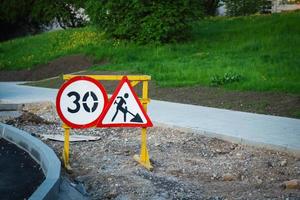 Señales de carretera de construcción con número y hombre de excavación con símbolo de pala en camino de arena en construcción foto