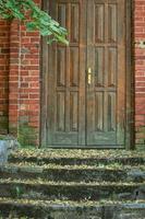 Old brown wooden door in red brick wall building with weathered green stairs photo