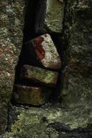 Old dirty bricks stacked in a hole between walls covered in moss photo