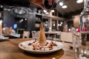 Man pouring caramel over delicious ice cream dessert on table at restaurant photo