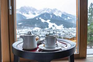 Ceramic tea kettle and cup with breakfast on table with mountains in background
