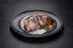 Canned sardine in oil on a black round plate against a dark concrete background photo