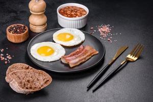 English breakfast with fried eggs, bacon, beans, tomatoes, spices and herbs photo