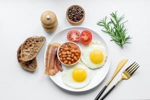 English breakfast with fried eggs, bacon, beans, tomatoes, spices and herbs photo