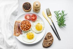 English breakfast with fried eggs, bacon, beans, tomatoes, spices and herbs photo