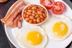 English breakfast with fried eggs, bacon, beans, tomatoes, spices and herbs photo