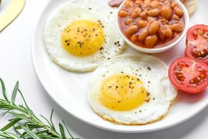 English breakfast with fried eggs, bacon, beans, tomatoes, spices and herbs photo