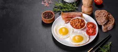 English breakfast with fried eggs, bacon, beans, tomatoes, spices and herbs photo