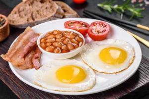 English breakfast with fried eggs, bacon, beans, tomatoes, spices and herbs photo