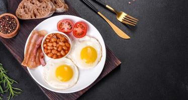 English breakfast with fried eggs, bacon, beans, tomatoes, spices and herbs photo