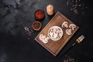 Beautiful young white champignons torn to slices on a dark concrete background photo